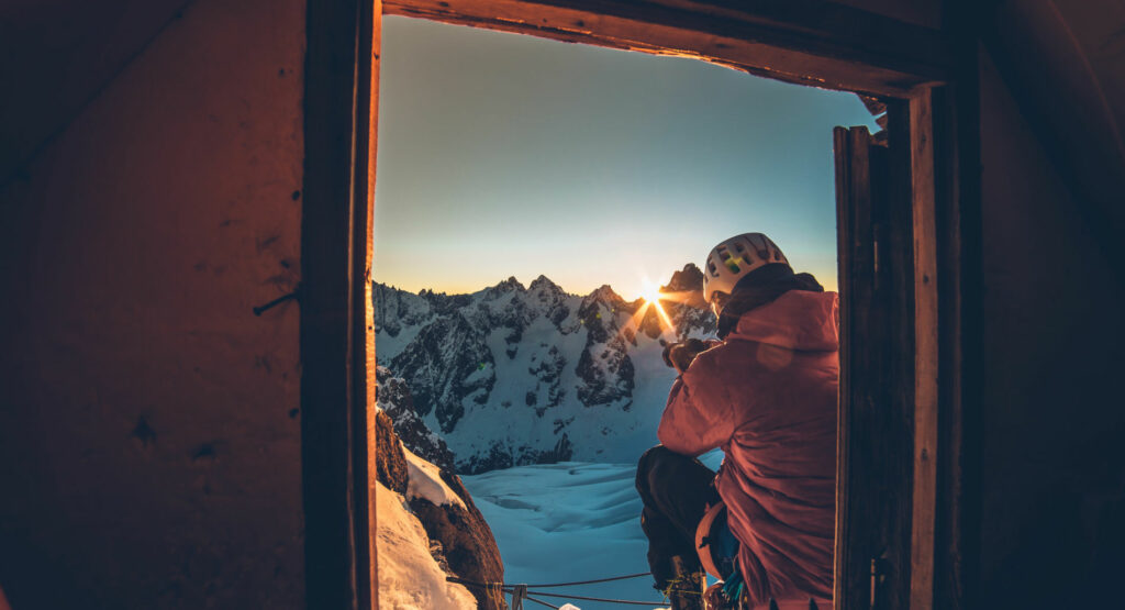 Un skieur de dos visible à travers une fenêtre entrain de prendre une photo de la montagne